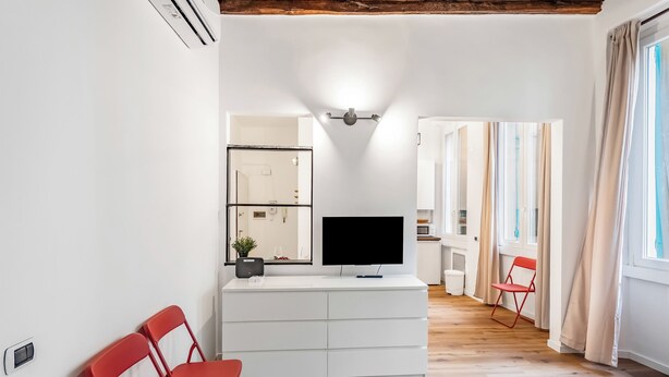 A modern living room with a flat-screen TV, a white cabinet, and a red chair. - Old Town Living in Historic Center & A/C (Genoa)