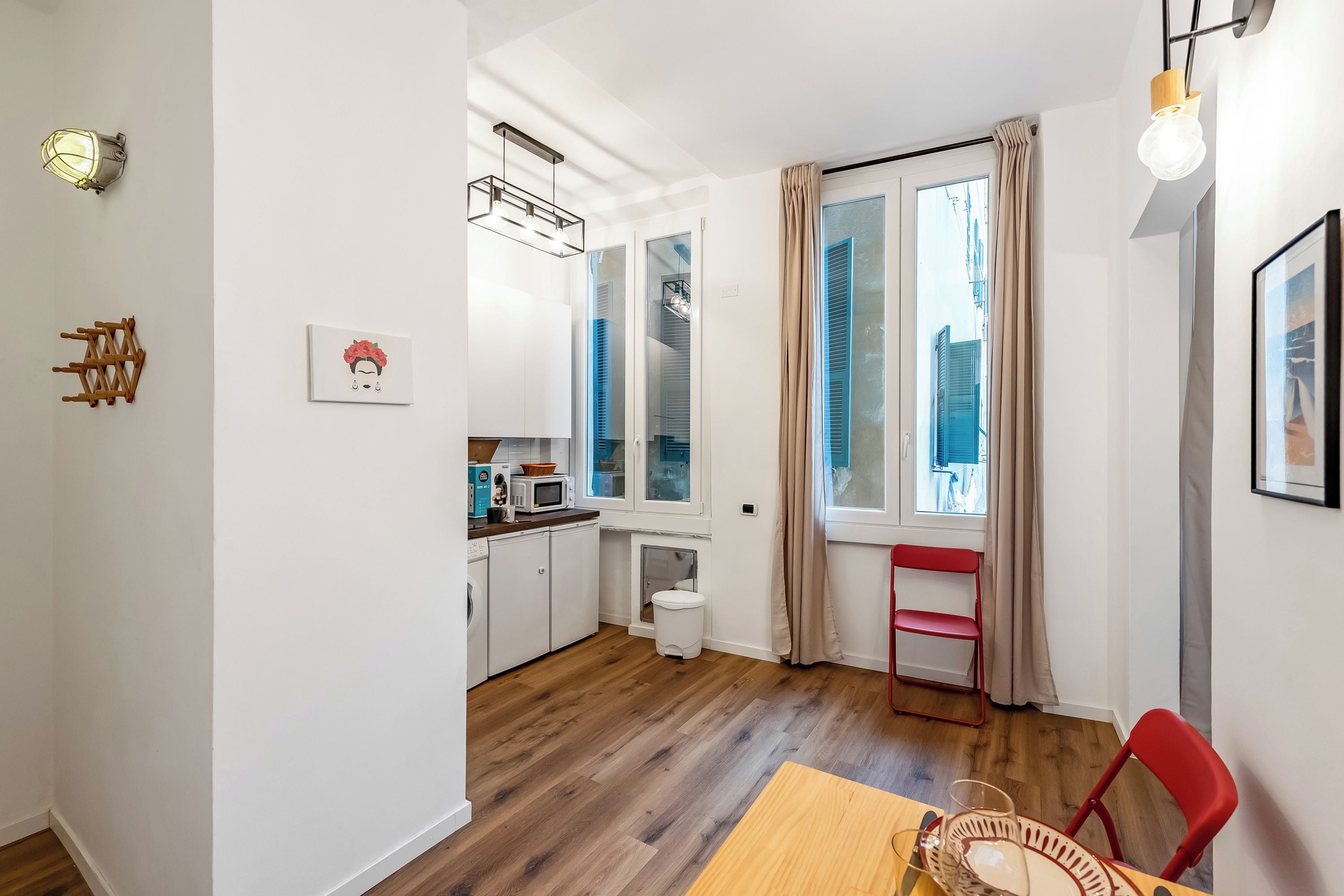 Une cuisine de taille réduite avec un coin repas, une chaise rouge et une fenêtre avec des rideaux.