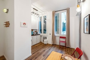 Cocina compacta con zona de comedor, una silla roja y una ventana con cortinas.