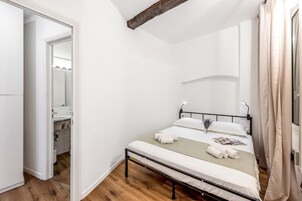Un dormitorio con cama, mesita de noche, espejo y ventana con cortinas.