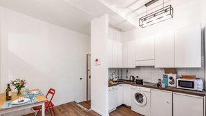A compact kitchen with white cabinets, a washing machine, a microwave, and a dining area with a table and chairs. - Old Town Living in Historic Center & A/C (Genoa)