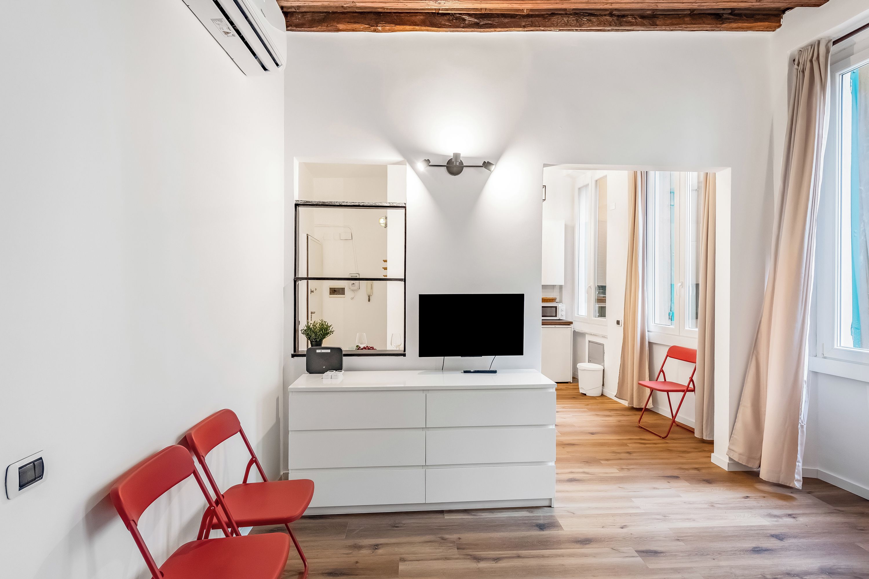 Un salon moderne avec un téléviseur à écran plat, un meuble blanc et un fauteuil rouge.