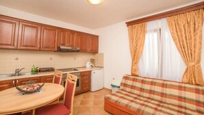 Eine kompakte Küche mit Holzausstattung, einem Esstisch mit Stühlen, einem kleinen Kühlschrank und einer Couch mit Karomuster.