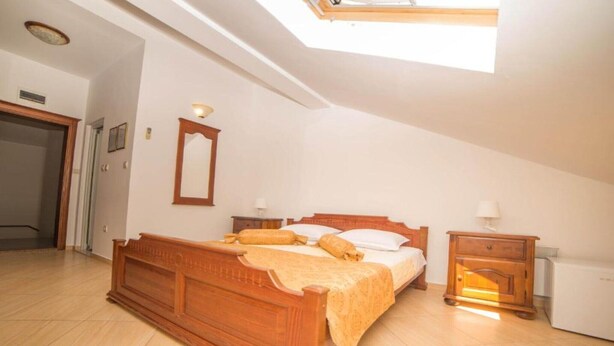 Ein Schlafzimmer mit einem hölzernen Bett, einem Nachttisch, einem Spiegel und einem Dachfenster.
