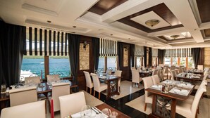 Ein Restaurant mit gedeckten Tischen, großen Fenstern mit Vorhängen und Blick auf das Wasser.