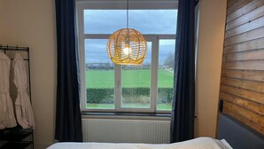 A bedroom with a large window, a hanging light fixture, and a bed with a white duvet.