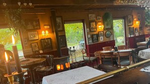 A cozy restaurant interior with wooden tables, chairs, and a central wood-burning stove.