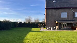 A residential property with a well-maintained lawn, a patio with outdoor furniture, and a brick house with a tiled roof.