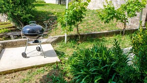 Una parrilla de barbacoa sobre una base de concreto en un jardín con césped y plantas pequeñas.