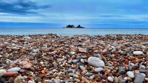 Ein Kiesstrand mit einem Felsen im Hintergrund.