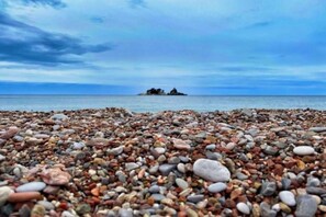 Ein Kiesstrand mit einem Felsen im Hintergrund.