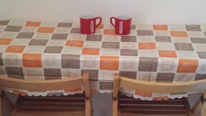 Ein Tisch mit karierter Tischdecke, zwei Holzstühle und zwei rote Tassen darauf.