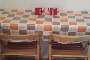 Ein Tisch mit karierter Tischdecke, zwei Holzstühle und zwei rote Tassen darauf.