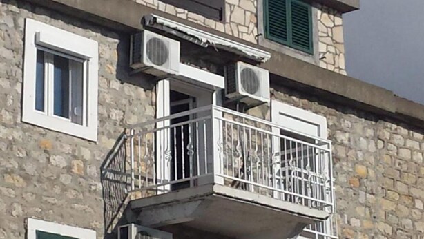 Ein Steinhaus mit Balkon, Klimaanlagen und Fensterläden.