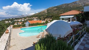 Una piscina con vista su un paesaggio montuoso, un'area salotto coperta e un edificio con tetto in tegole rosse.