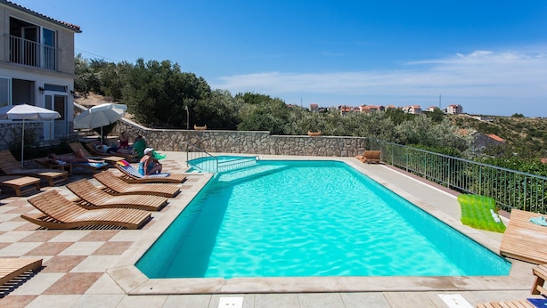 Una piscina con lettini e ombrelloni, circondata da un muro in pietra e con vista su un pendio collinare.