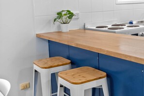 Cocina con encimera de madera, dos taburetes blancos y una estufa.
