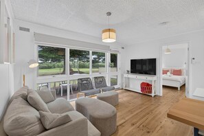 Ein modernes Wohnzimmer mit großem Fernseher, bequemen Sitzmöglichkeiten und Blick ins Freie.
