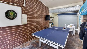 Una habitación con mesa de ping pong, dardo y pared de ladrillo.