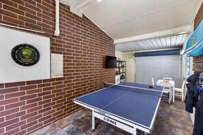 Ein Raum mit Tischtennisplatte, Dartscheibe und Backsteinwand.