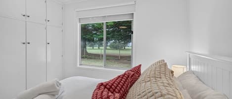 A bedroom with a large window, white walls, and a bed with rolled white towels.