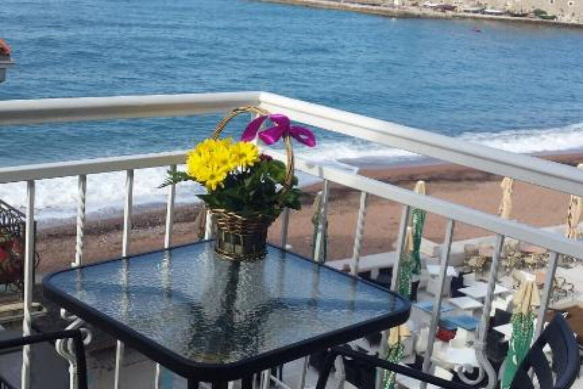 Un balcon avec une petite table sur laquelle est posé un panier de fleurs, donnant sur une plage et la mer.