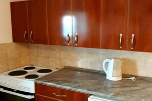 A kitchen with wooden cabinets, a stove, and a kettle on the countertop. - Villa Teodora Mare - Family Suite with Balcony (App 1) (Petrovac na Moru)