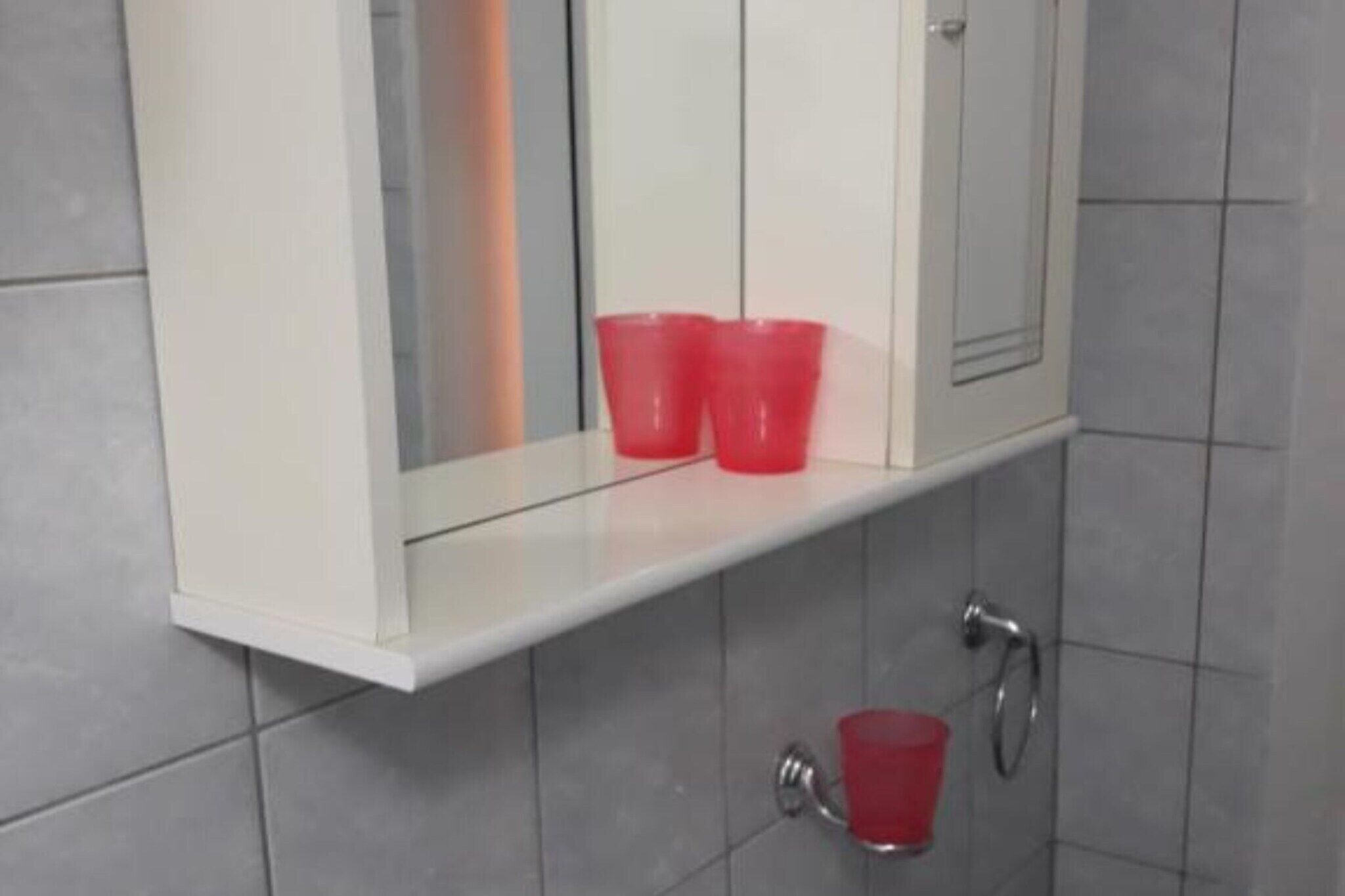 A bathroom with a white vanity, two red cups on the vanity, and a red cup on the floor.