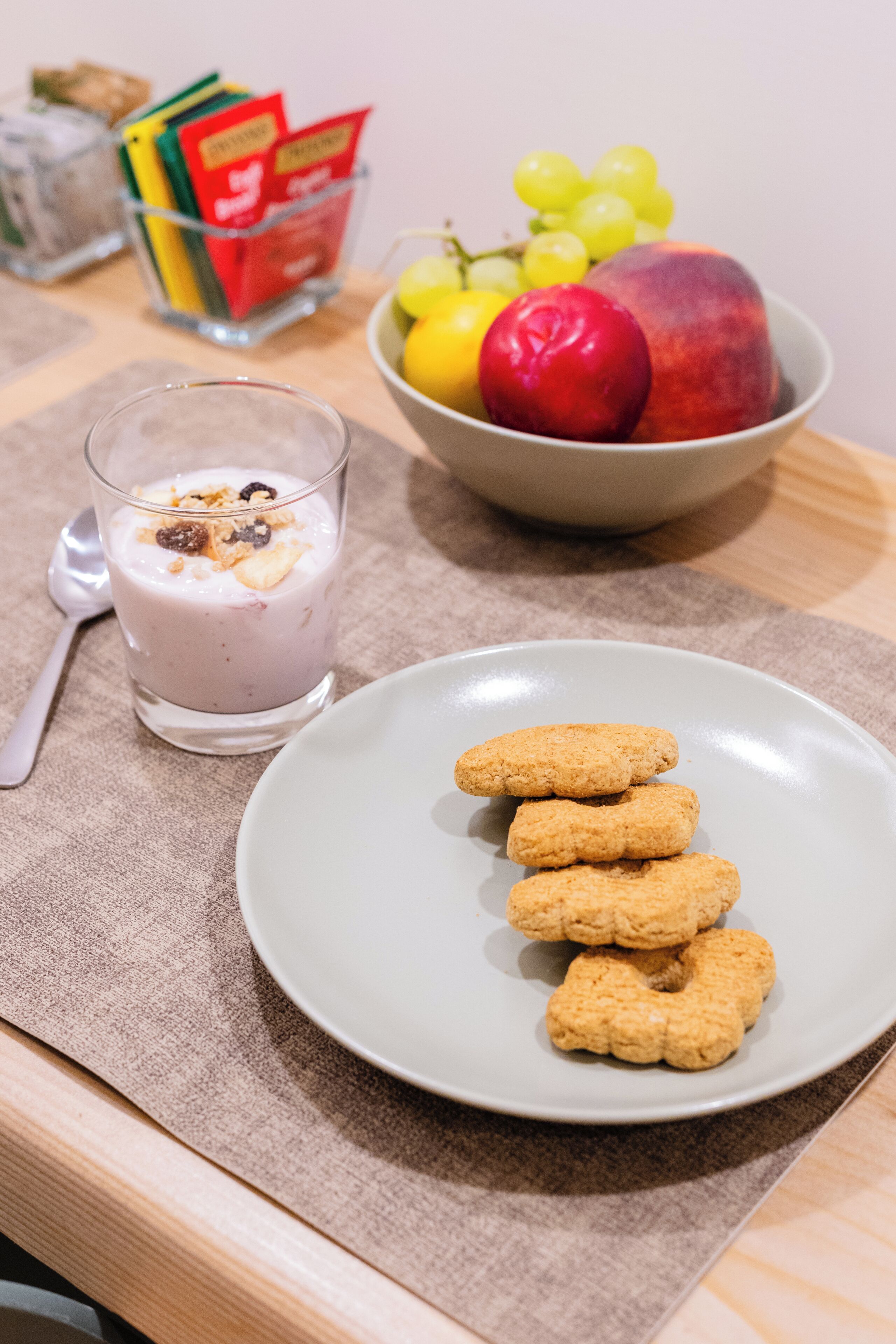 A table with a glass of yogurt, a bowl of fruit, and a plate of cookies.