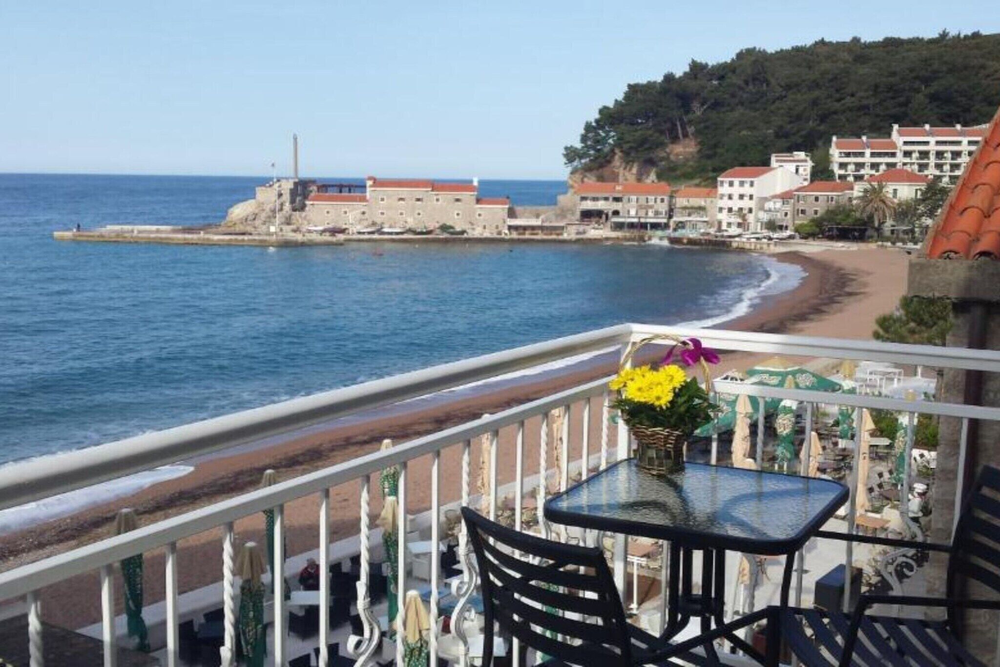 Un balcó amb taula i cadires que dona a una platja i un edifici històric.