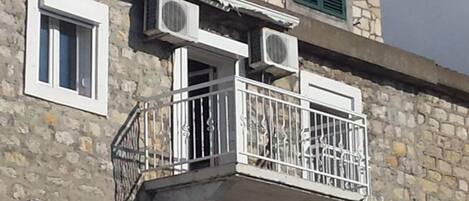 A stone building with a balcony, air conditioning units, and shutters.