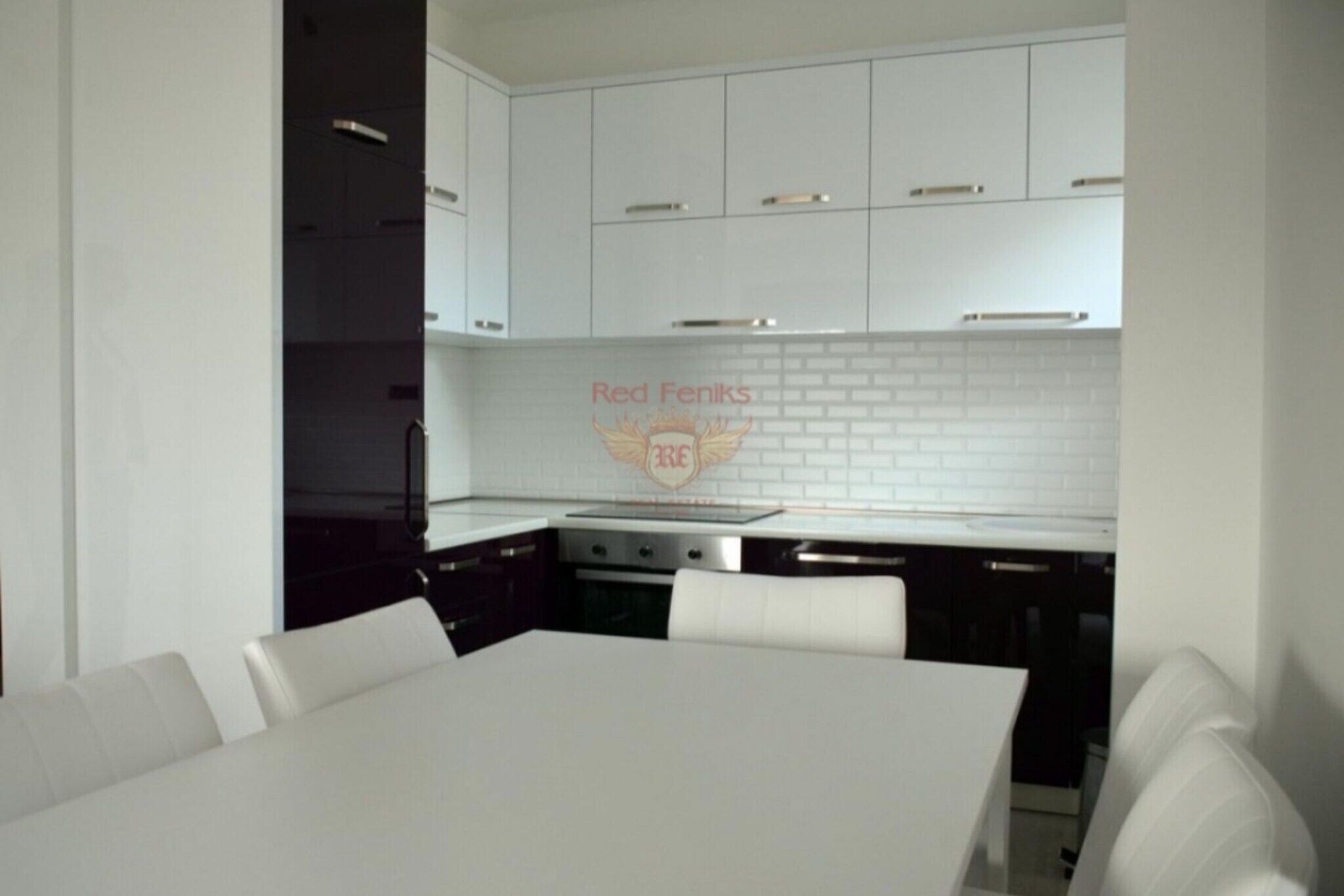 Una cocina moderna con armarios blancos, una isla central y un comedor con mesa y sillas blancas.