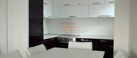 Una cocina moderna con armarios blancos, una isla central y un comedor con mesa y sillas blancas.