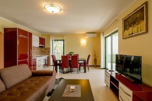 A compact living space with a sofa, dining table, chairs, a TV, and a kitchen area. - Amor Residence - Two Bedroom Apartment with Terrace and Sea View ( 7 ) (Herceg Novi)