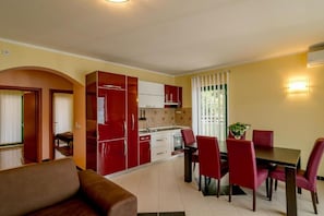 Een kleine keuken met moderne apparaten, een zithoek met rode stoelen en een loungehoek met een bruine bank.