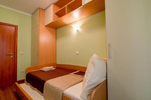 Een kleine slaapkamer met een enkel bed, een houten garderobe en een inbouwkast boven het bed.