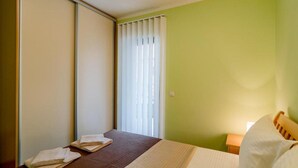 Hotellihuone, jossa on sänky, yöpöytä, ikkuna, jossa on sälekaihtimet, ja liukuovi.