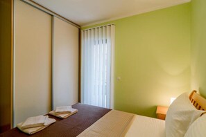 Ein Hotelzimmer mit Bett, Nachttisch, Fenster mit Jalousien und einer Schiebetür.