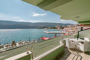 Ein Balkon mit Seeblick, eine Pier mit Sonnenschirmen und Gebäude im Hintergrund.