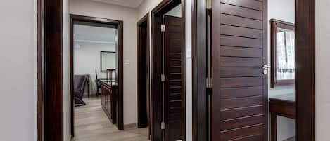 A hallway with wooden doors, a seating area with a table, and a view of a room with a window.