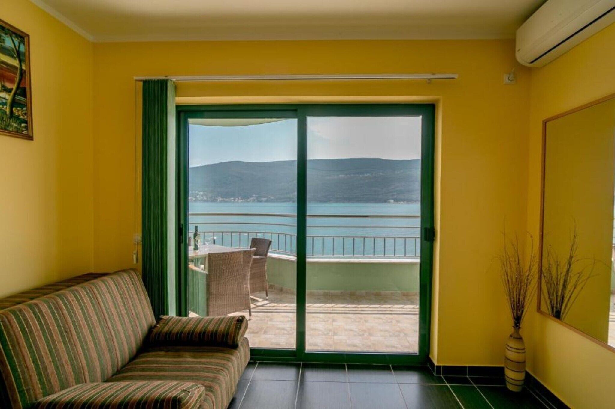 Une pièce avec un canapé, une porte-fenêtre coulissante donnant sur un balcon avec vue sur la mer et les collines.