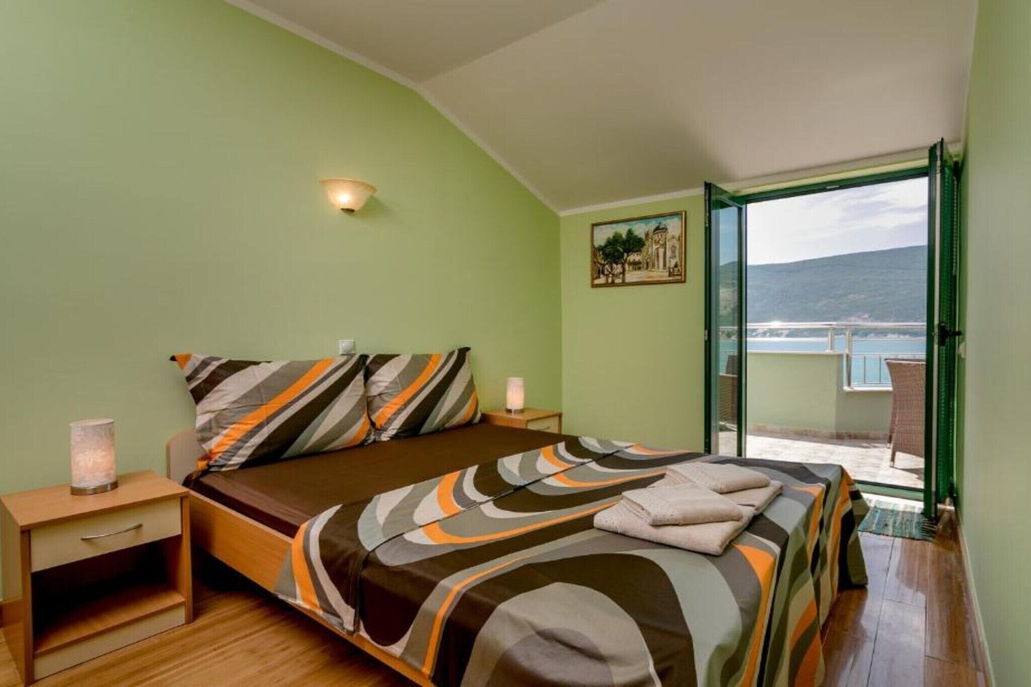 A bedroom with a bed, bedside tables, a lamp, and a view of the sea.