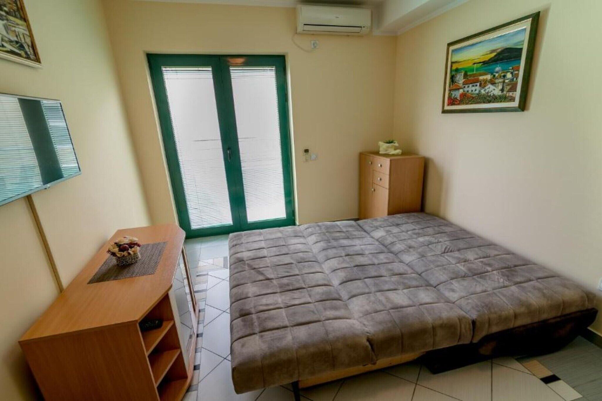 A bedroom with a bed, a desk, a cabinet, a window with blinds, and a painting on the wall.
