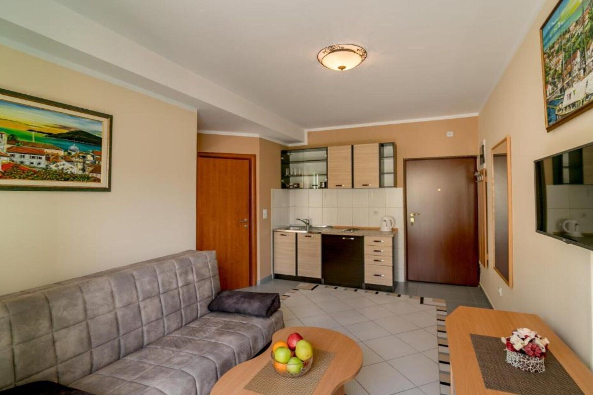Un espacio habitable compacto con sofá, una pequeña mesa de comedor con fruta, una zona de cocina y un televisor en la pared.