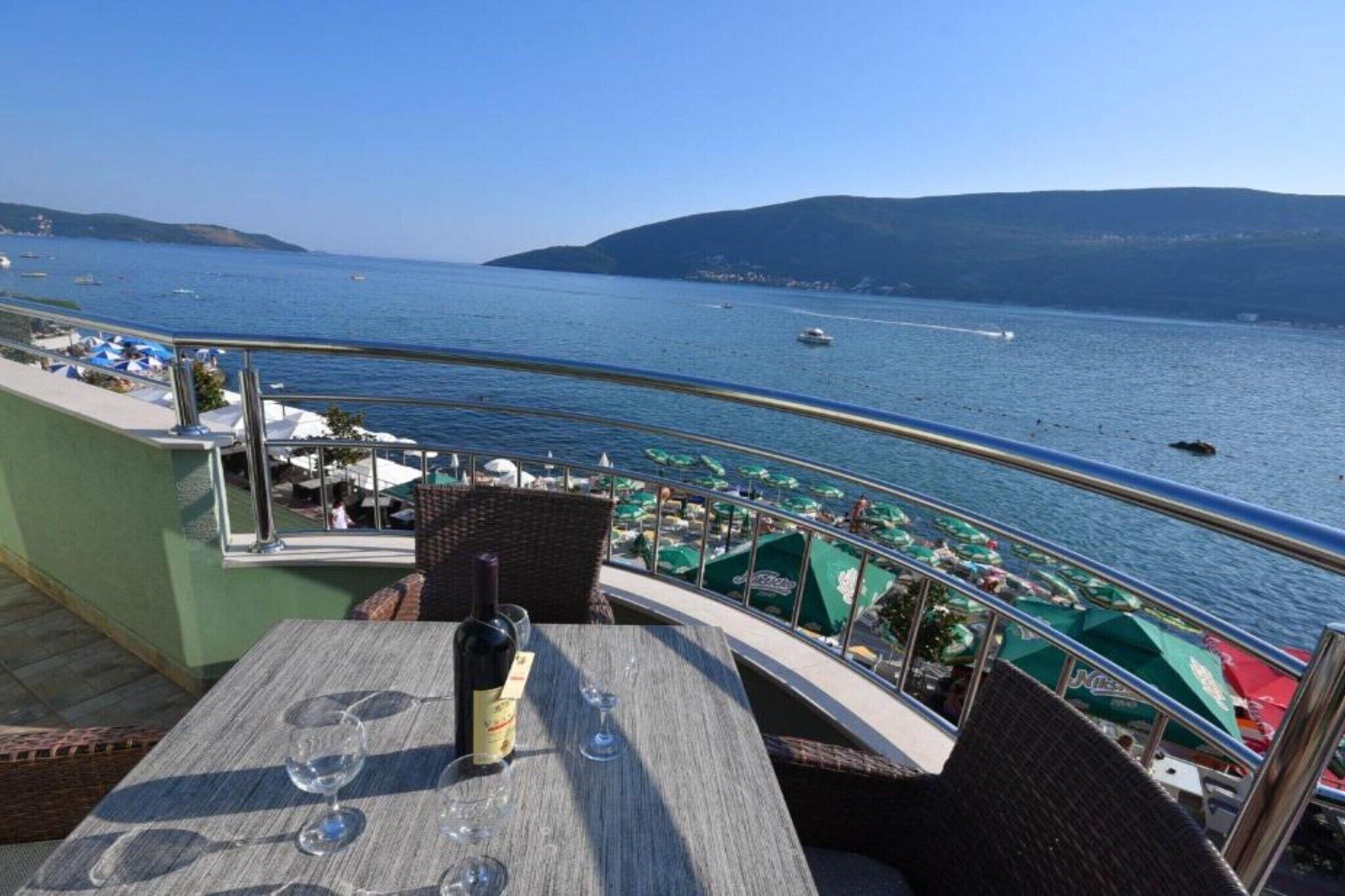 Una terraza con una mesa preparada para dos, con vista a un puerto deportivo con barcos y una vista despejada del mar.