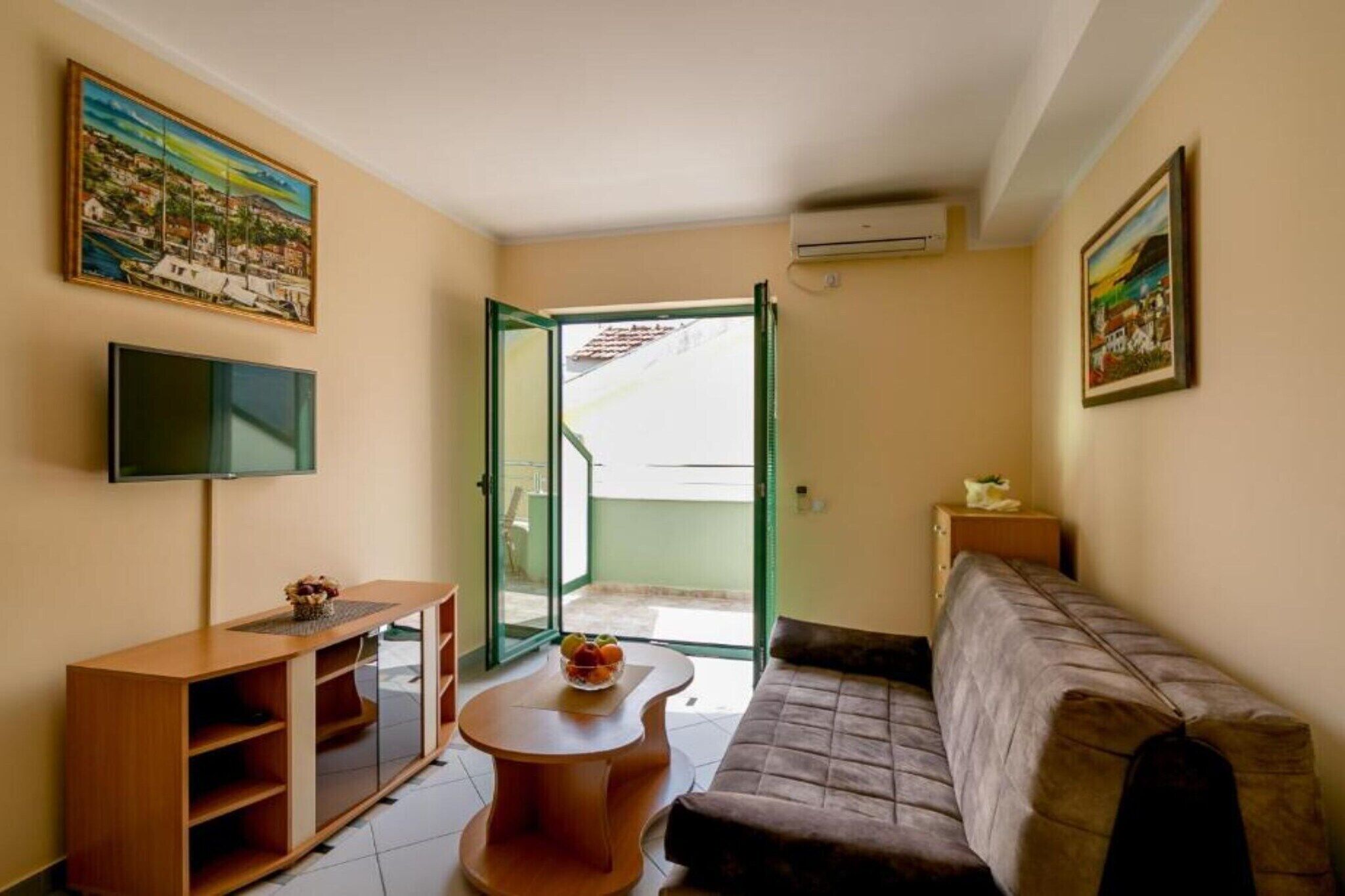 A living room with a sofa, a TV, a wooden cabinet, a glass door leading outside, and a small table with fruit.