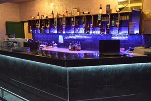 Una zona de bar con mostrador, estantes llenos de botellas, vasos y un ordenador portátil.