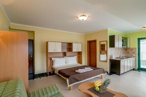 A hotel room with a bed, a small table with fruits, a kitchenette, and a green door. - Amor Residence - Studio Apartment with Terrace and Sea View (4 ) (Herceg Novi)