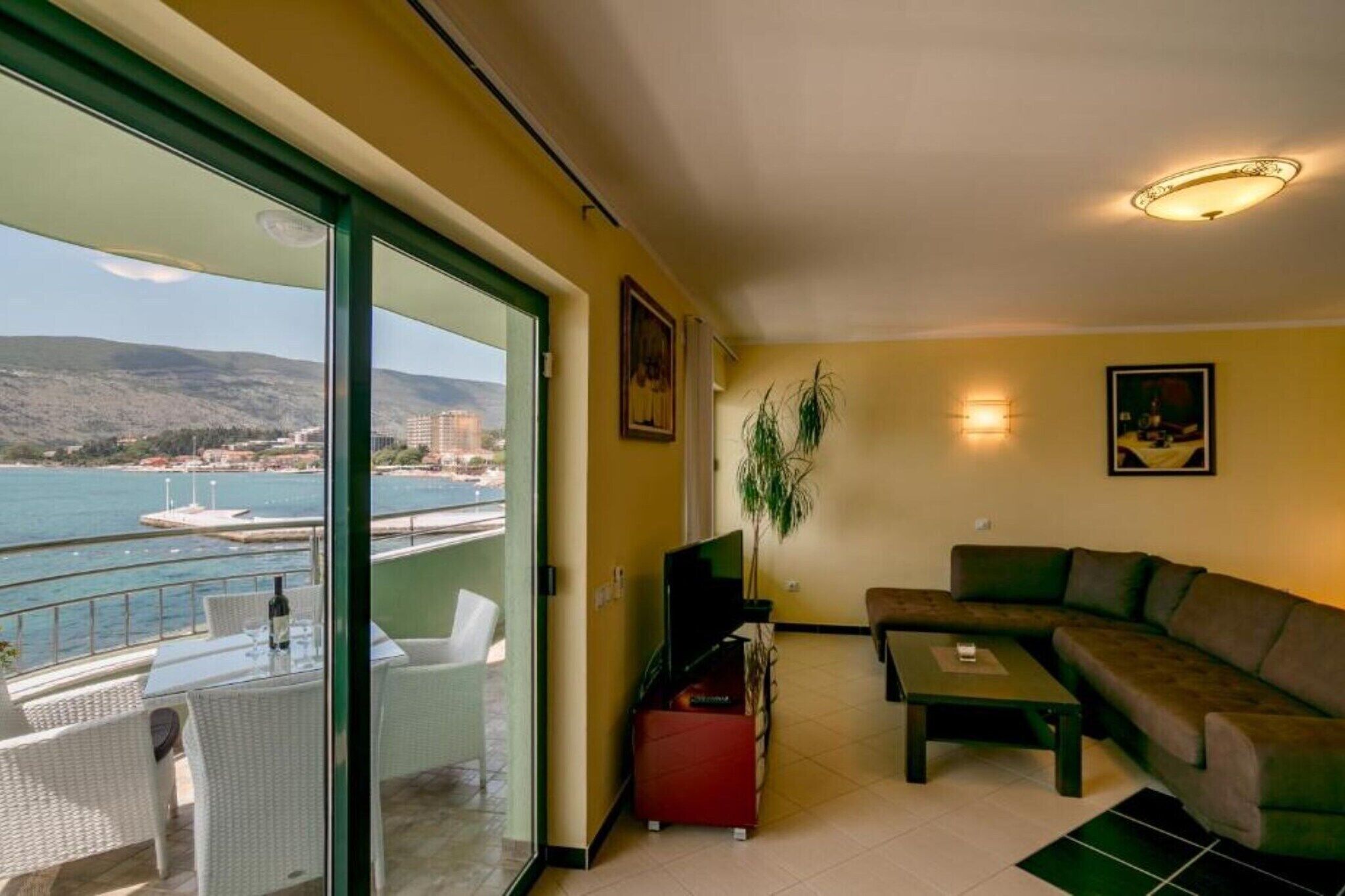 Una sala de estar con sofá, mesa de centro y televisor. Hay un balcón con vistas al mar y a edificios.