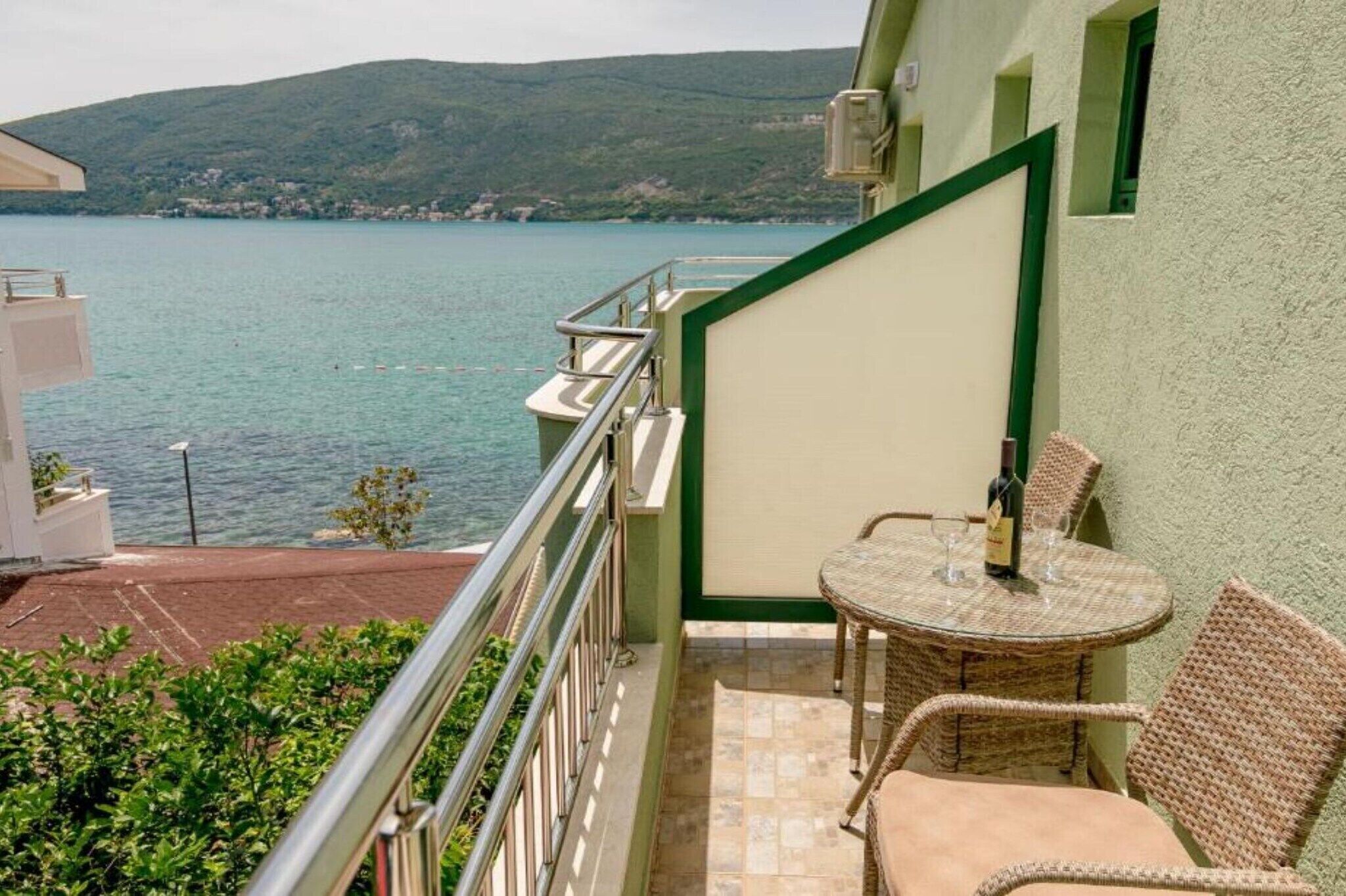 Ein Balkon mit Tisch und Stühlen, mit Blick auf ein Gewässer und Hügel.